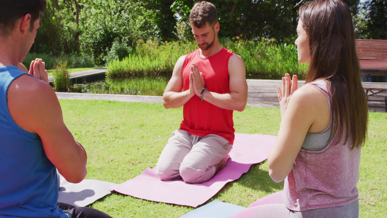 grupo feliz practicando postura de yoga arrodillado en esteras en un parque soleado
