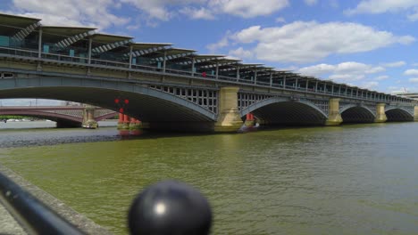 POV-Ansicht-Der-Londoner-Themse-Eisenbahn-über-Den-Fluss-Im-Zentrum,-Schmutziges-Grünes-Wasser,-Eine-Weitere-Brücke-Im-Hintergrund,-Filmische-Szenerie,-Teilweise-Bewölkter-Sommer