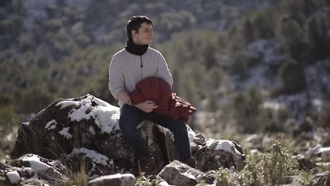 Traveler-resting-on-snowy-stone-against-mount