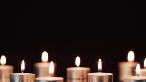 Video-of-rows-of-tea-candles-with-white-flames-and-copy-space-on-black-background