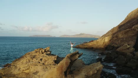 adventure woman with arms up stands on jagged rock on coast of porto santo