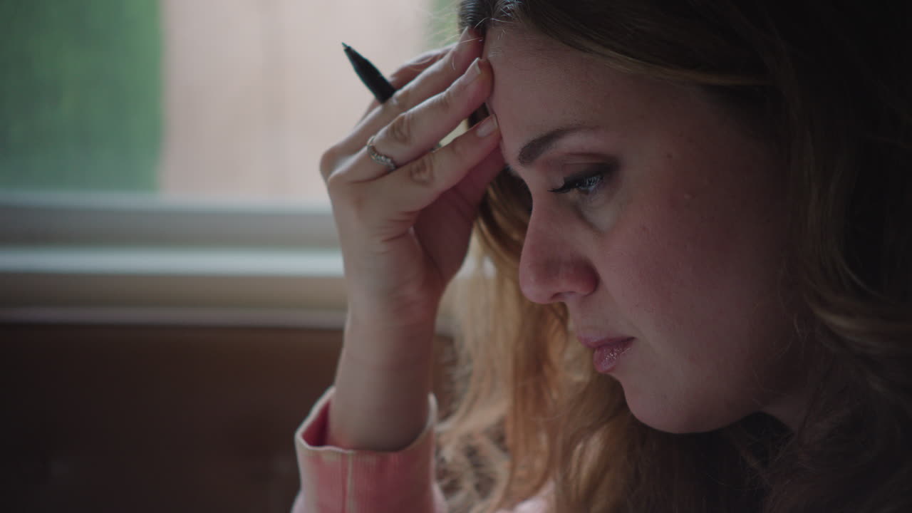 toma de mano de una mujer estresada sosteniendo un bolígrafo en la mesa, contemplando y pensativa al lado de la ventana durante el día