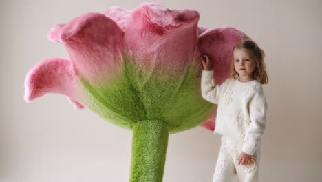 young girl standing next to an oversized plush pink and green flower