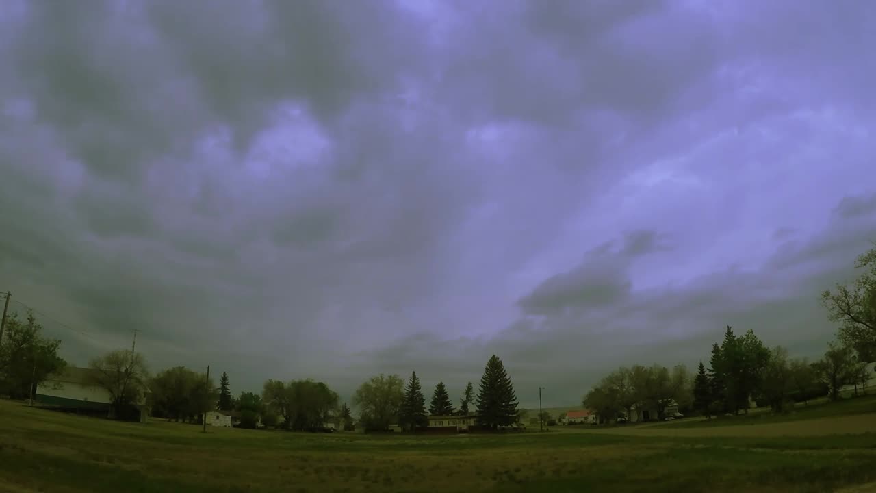시간 경과 - 먼 거리에 있는 부부의 집이 있는 신선한 녹색 풀밭 위에 보라색 색조의 구름