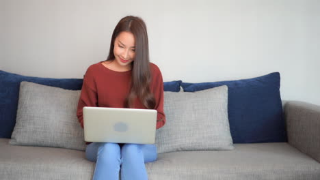 a young woman works diligently on her laptop while sitting comfortably on a large sofa