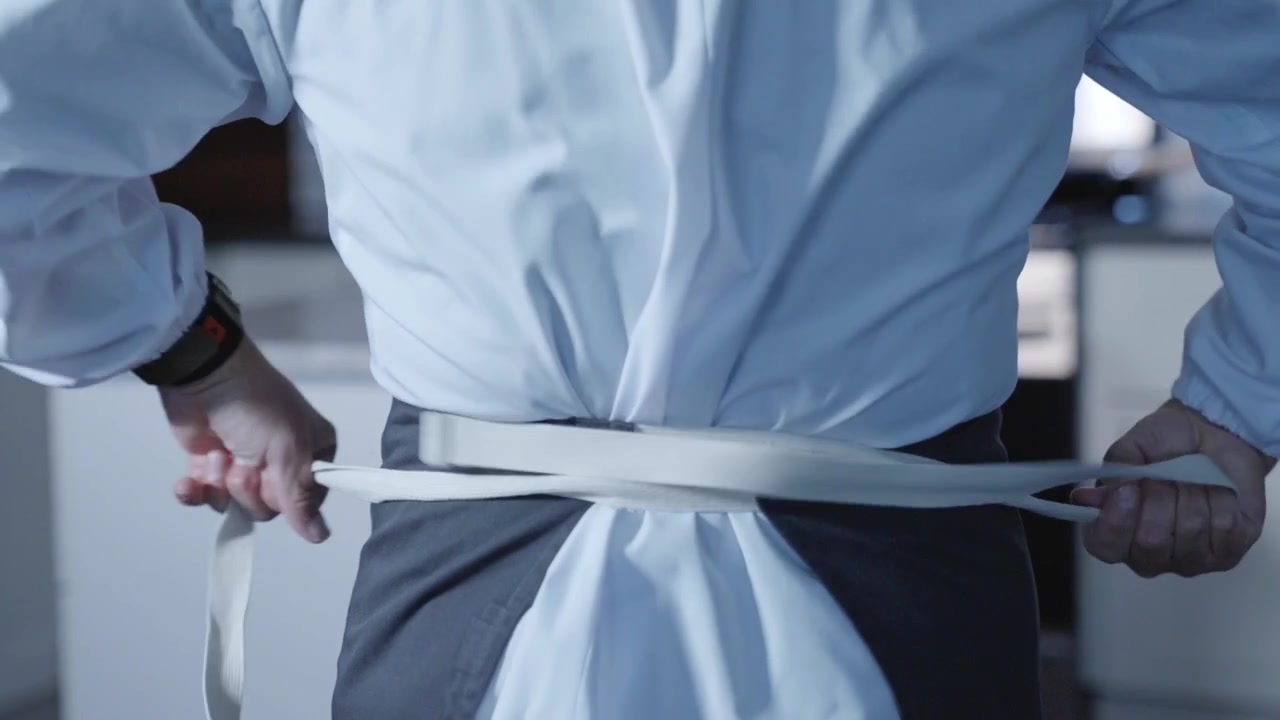 Um close-up captura um chef de sushi amarrando seu avental e uniforme, enfatizando a atenção aos detalhes e a preparação. Ideal para conteúdo culinário focado na preparação de sushi e na prontidão da cozinha