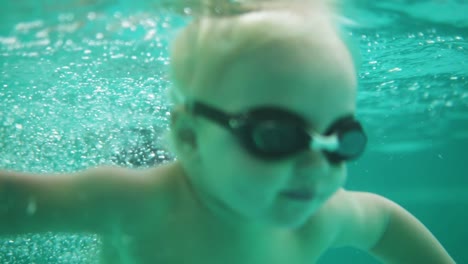 an underwater shot of a cute blonde toddler in protective glasses swimming under the water in the swimming pool. slowmotion