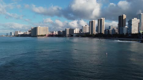 4K-cinematic-drone-shot-of-Waikiki-Beach-and-hotels-from-right-over-the-water-as-waves-crash-in-Oahu