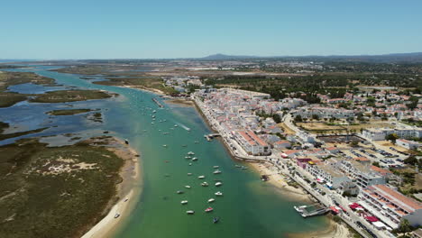 boats floating on calm river with waterfront buildings in cabanas de tavira, portugal