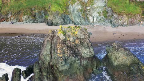 aerial orbit view of a colourful rock along the south coast of ireland with waves braking around it