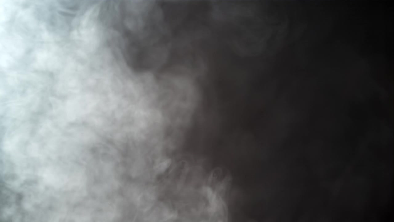 Fumo bianco in movimento lento che si diffonde su uno sfondo scuro.