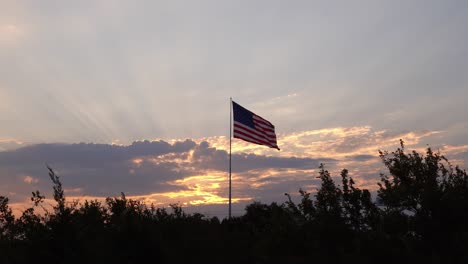 yellow sunset rays in pink blue sky behind clouds frame patriotic waving american flag