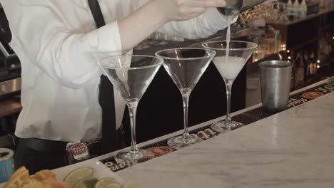 upscale bartender mixologist pours alcoholic drink into martini cocktail glass