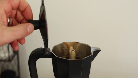 A-person-lifts-the-lid-on-a-stovetop-espresso-maker-to-show-the-coffee-pouring-out