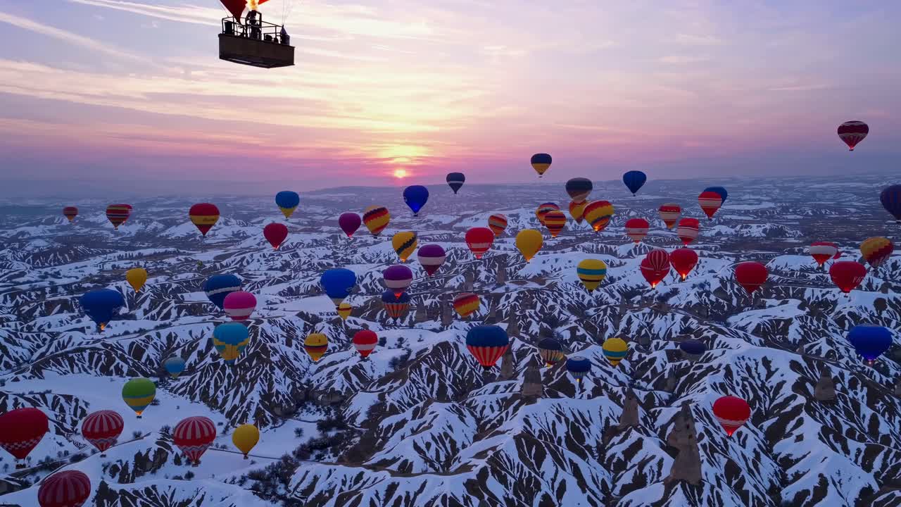 Aerial video captures vibrant hot air balloons over snowy landscapes at sunrise