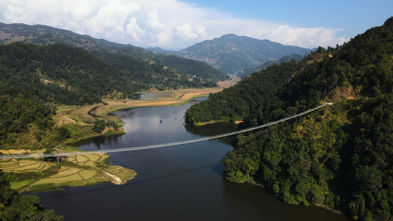A Scenic View of Rupa Lake With a Suspension Bridge Framed by the Majestic Machhapuchhre in Kaski District, Nepal - Aerial Drone Shot