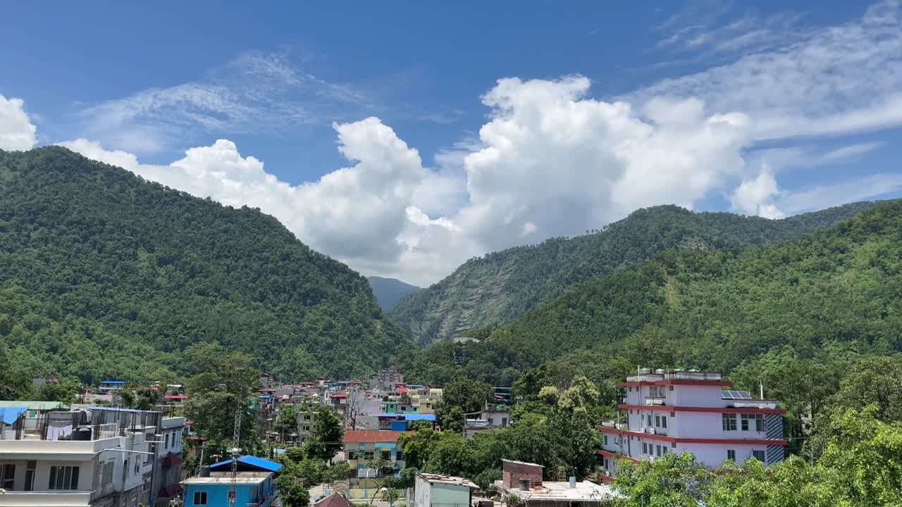 Scenic aerial view of Bandipur hill town surrounded by lush green mountains and vibrant houses under bright blue sky with fluffy clouds showing peaceful beauty of Nepal Outdoors