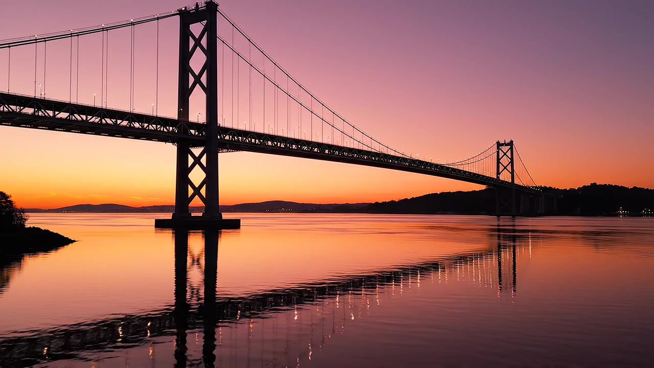Ponte sospeso al tramonto su acqua calma con cielo arancione