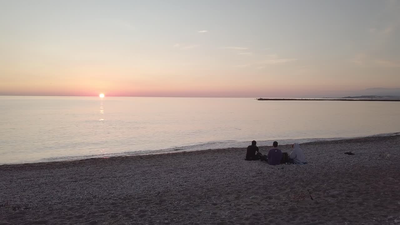 three friends sitting on the beach watching the sunset