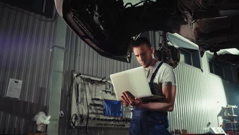 auto mechanic inspecting car undercarriage with laptop