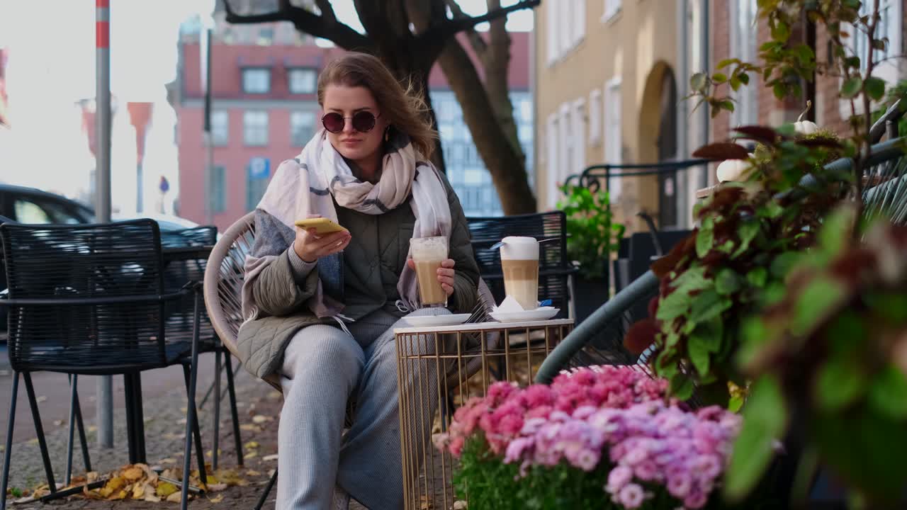 Woman enjoying coffee and phone in an autumn cafe