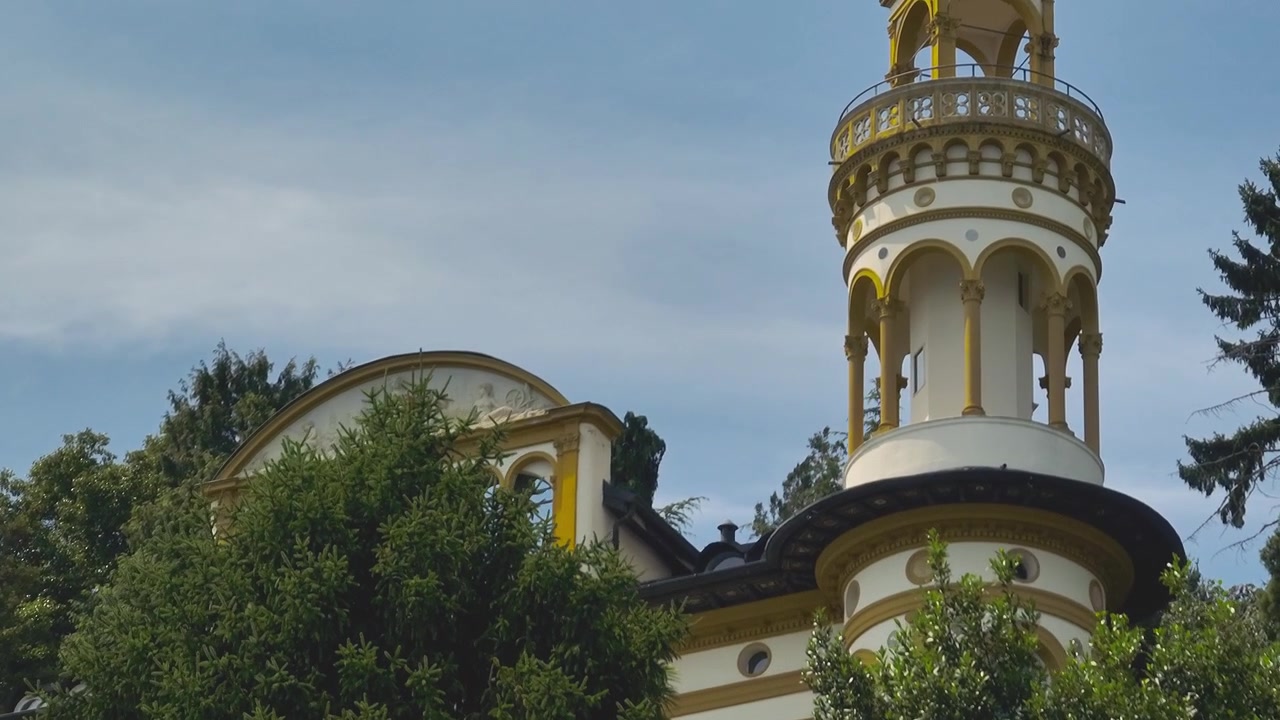 Close-up de drone de detalhes elegantes de colunas redondas em uma torre de vila histórica italiana à beira do lago, contra um céu azul claro com pássaros voando, destacando arquitetura atemporal e artesanato refinado