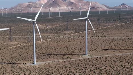 aerial view panning across wind turbines slowly rotating in the mojave desert sunlight against mountain landscape