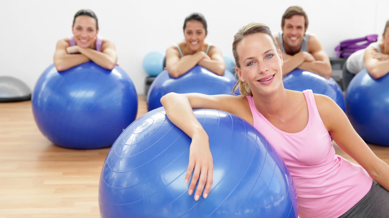 clase de fitness apoyándose en bolas de ejercicio sonriendo a la cámara