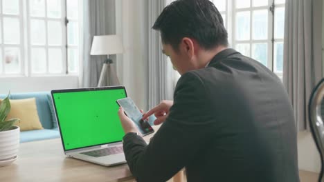 Asian Businessman Wearing Business Suit With Green Screen Computer Using Mobile Phone While Working At Home.