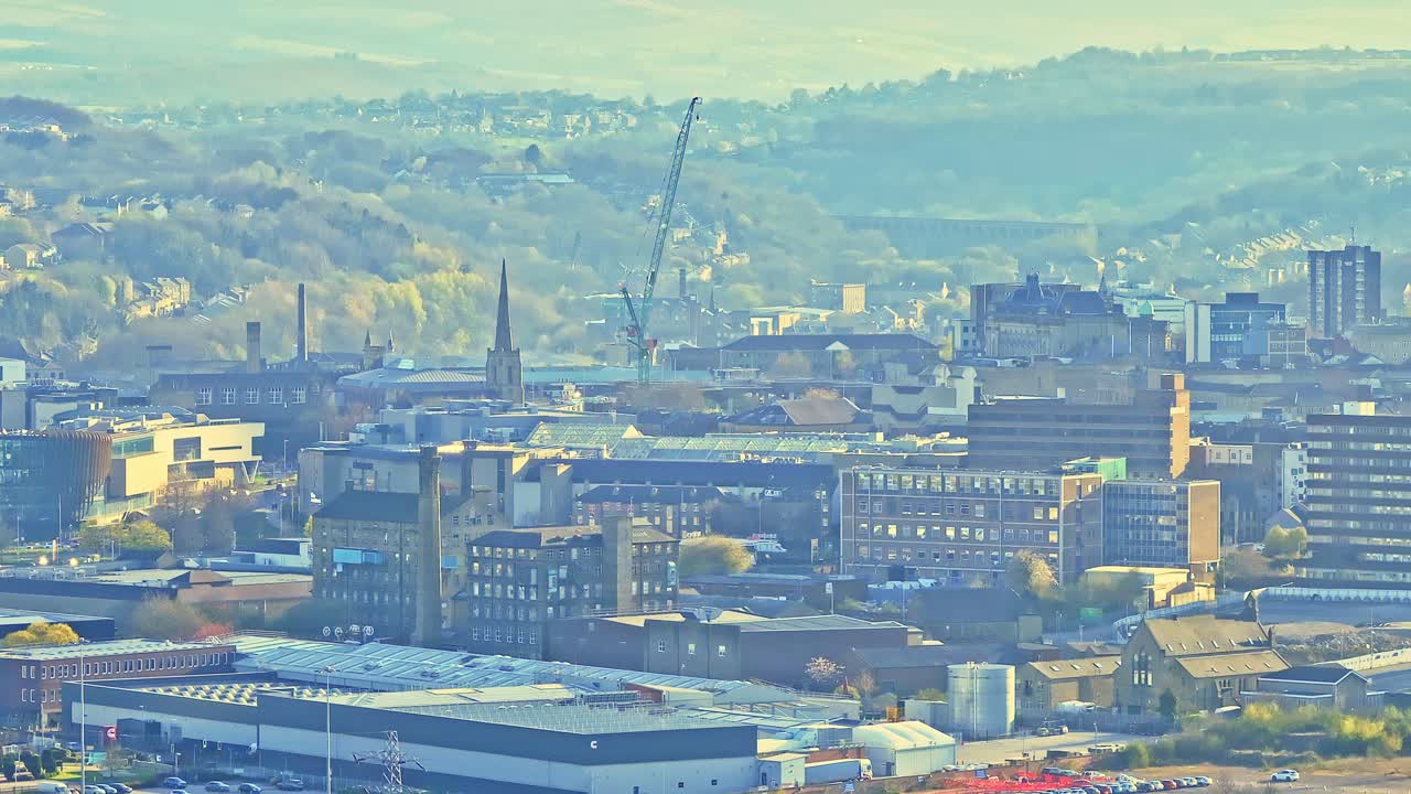 Huddersfield town football club area revealing stadium surroundings, industrial buildings, dense urban skyline, and distant rolling hills under soft light, static drone shot