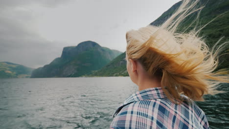 a free woman stands with her hands to the sides on the bow of a cruise ship traveling the fjords of