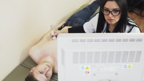 Young-beautiful-female-doctor-with-long-hair-in-glasses-is-screaning-her-patient's-heart-with-ultrasonography,-looking-at-the-screen.-Healthcare-and-medicine.