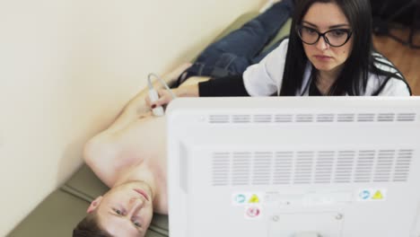 Young beautiful female doctor with long hair in glasses is screaning her patient&#039;s heart with ultrasonography, looking at the screen. Healthcare and medicine.