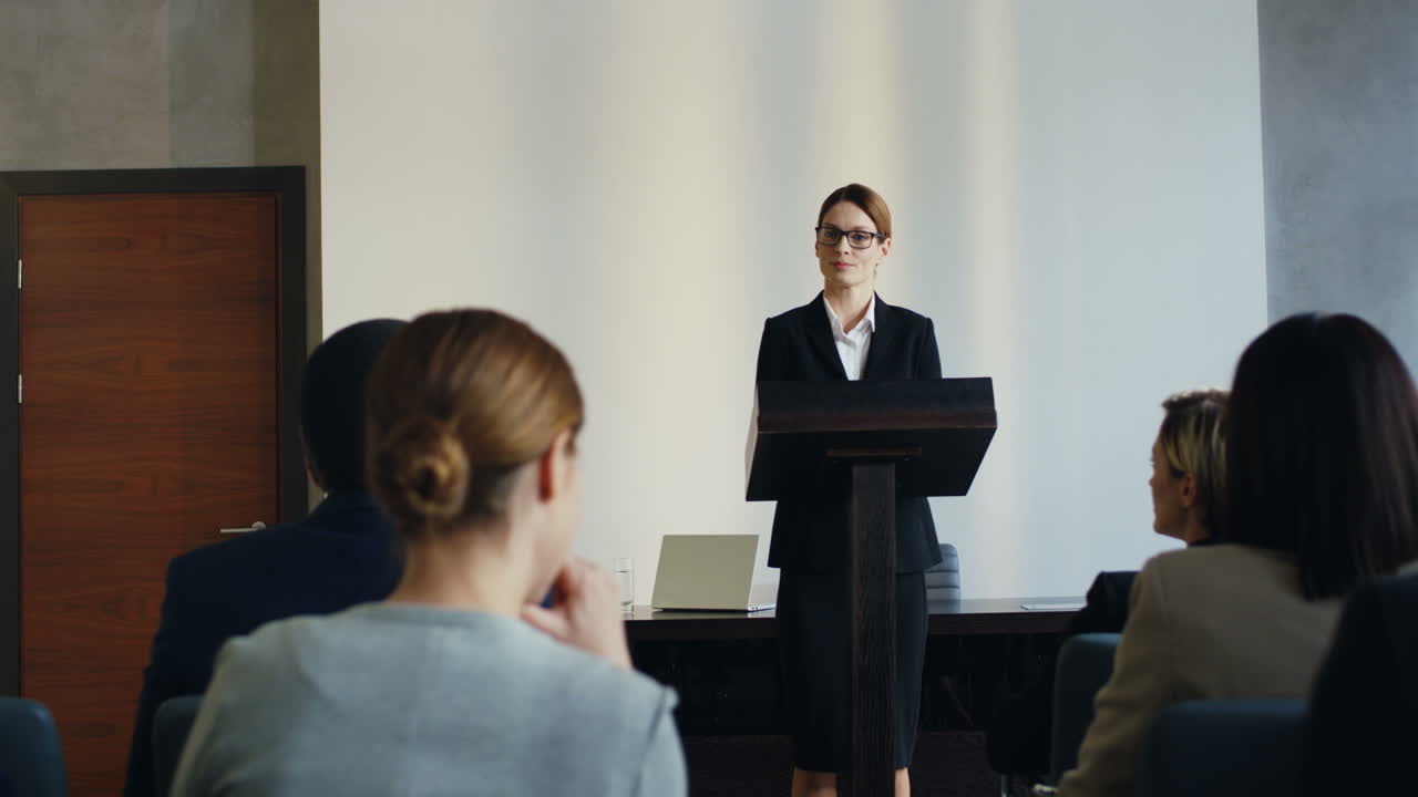 Caucasian female speaker on a podium making a speech at a conference and answering questions from the auditory