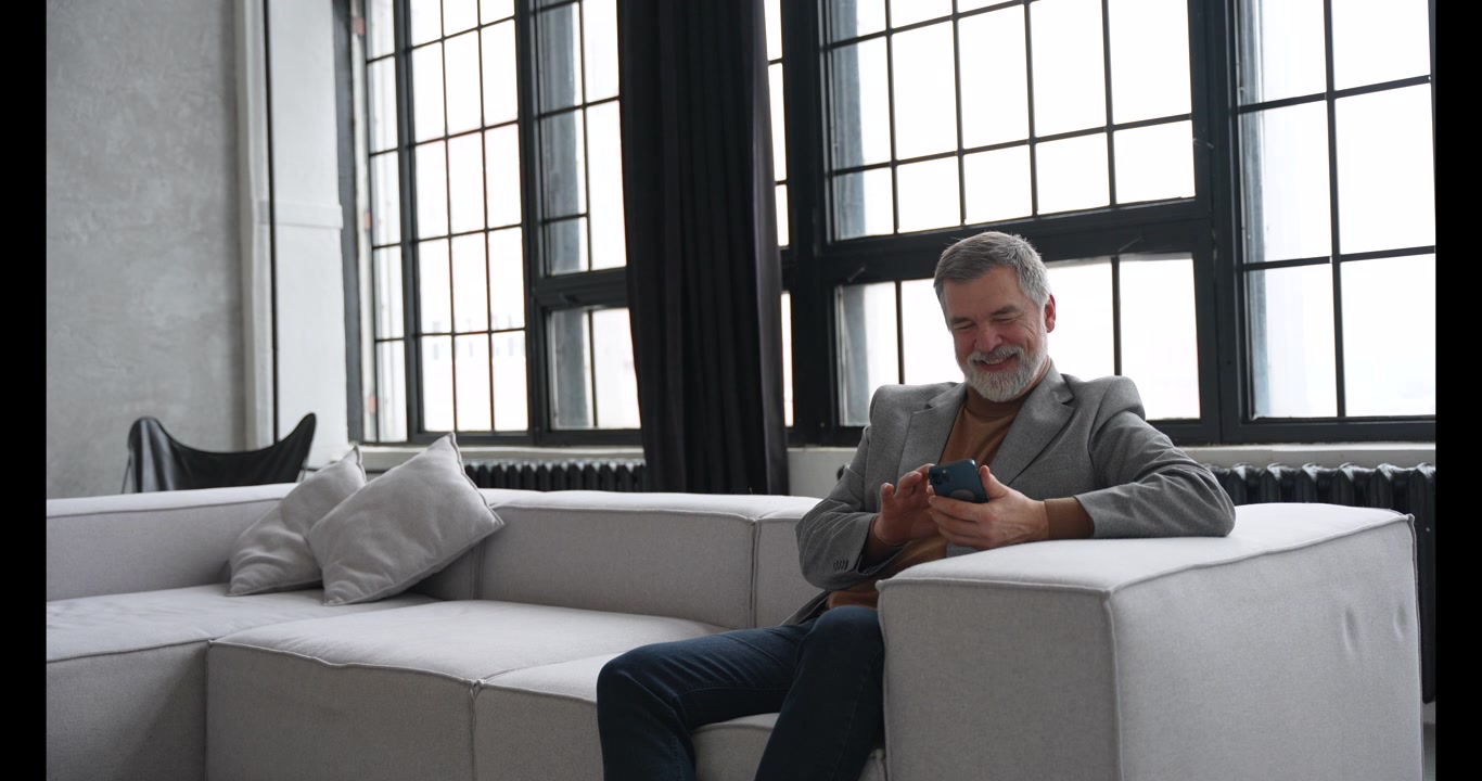 Mature Businessman Using Smartphone While Sitting on Sofa in Modern Office