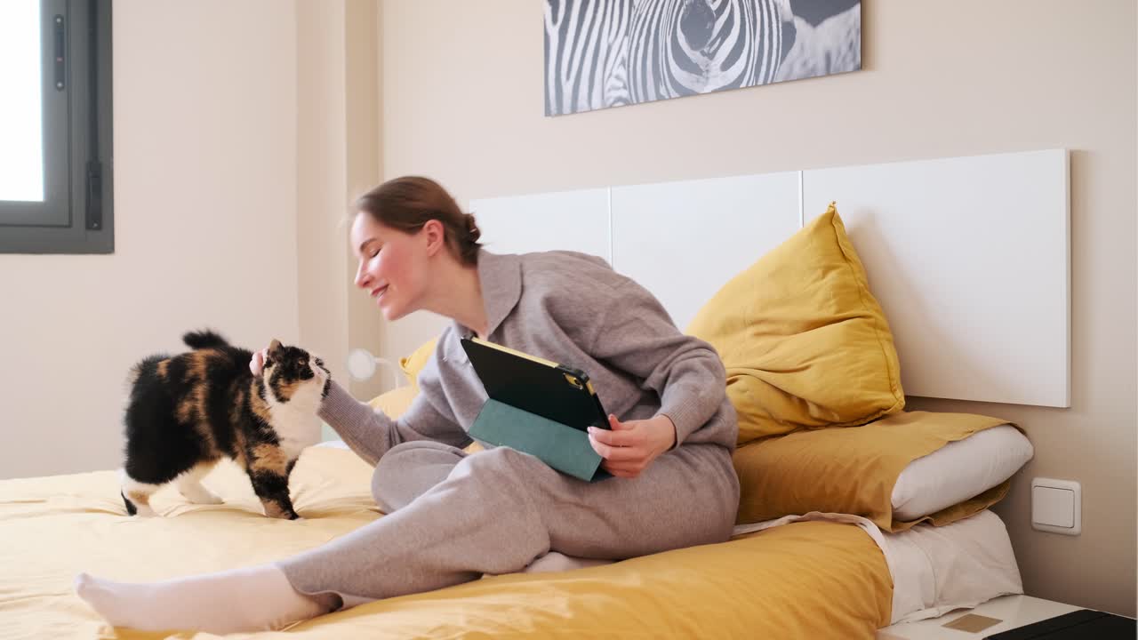 Woman petting her cat in bed while using a tablet