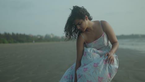 una joven india está de pie en una playa con un vestido azul.