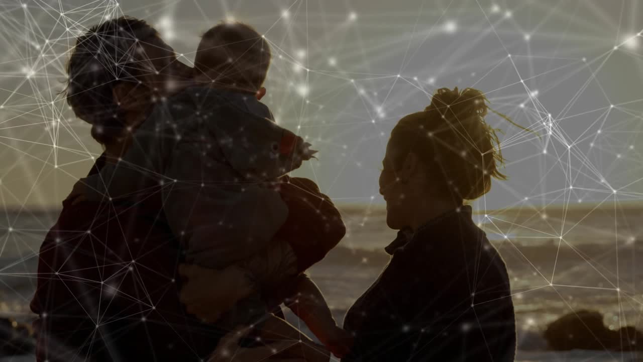 Father lifting infant to mother on shore at sunset, kissing to bond under tech overlay shifting