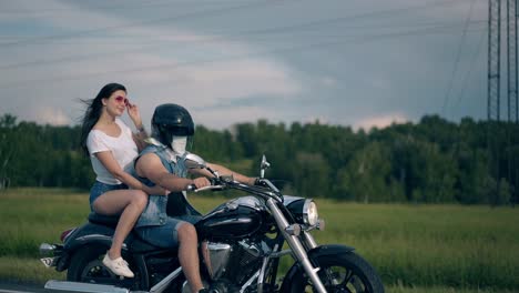 young couple rides motorcycle fast against dense forest