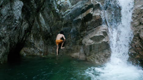 man exits the water to rope climb the rocky waterfall cliff, aerial