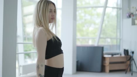 fit girl in black clothes performing contemporary. female dancer shows flowing motions, body and hands waves at white room. modern ballet dance choreography. young woman is moving smoothly