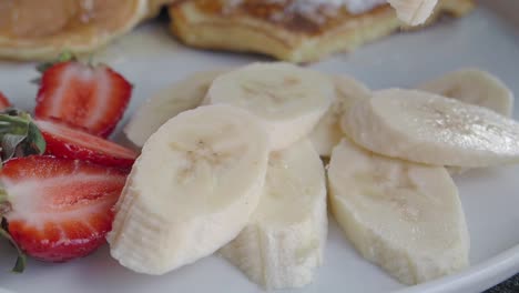 close up of banana slices with strawberries and pancakes on a plate