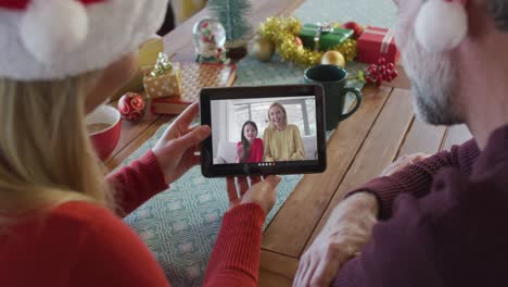 Pareja-Caucásica-Con-Sombreros-De-Santa-Usando-Tableta-Para-Videollamada-Navideña-Con-Familia-En-Pantalla