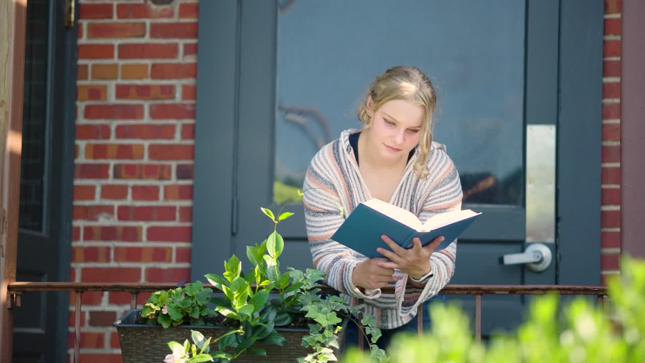 Girl student reading book over a side rail outside of a door