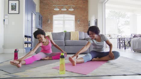 happy african american mother and daughter doing yoga in living room, stretching