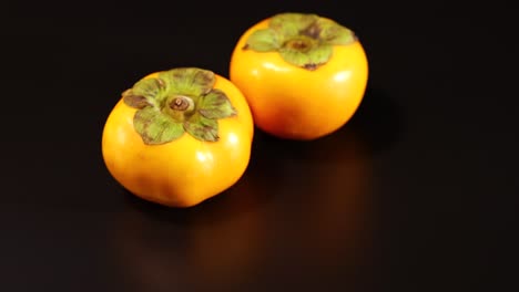 two persimmons resting on a dark background