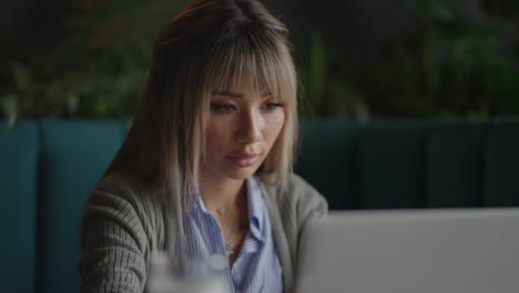 joven hermosa mujer de negocios asiática sonriente sosteniendo un café y una computadora portátil colocada en la mesa de madera en la oficina. mujer chequeando el correo o investigando mientras teletrabaja