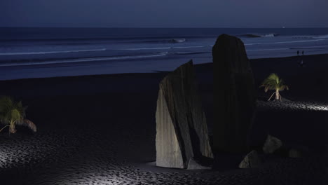 Night Beach Scene with Illuminated Rocks, Palm Trees, and Ocean Waves