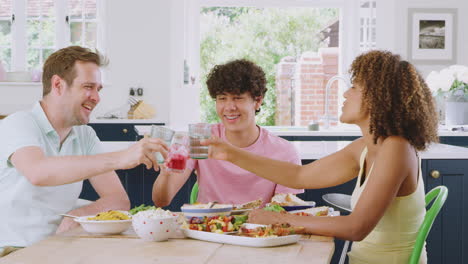 familia multirracial con un hijo adolescente sentado alrededor de la mesa en la cocina en casa comiendo juntos