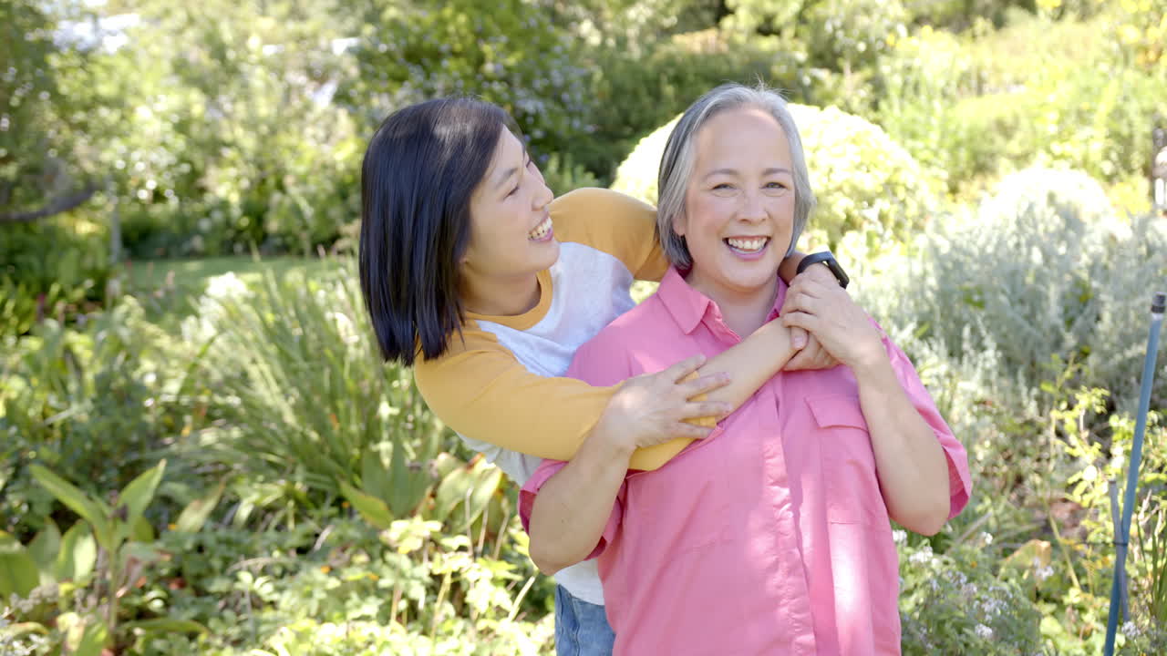 Smiling asian woman hugging senior asian woman in garden, enjoying outdoor time together